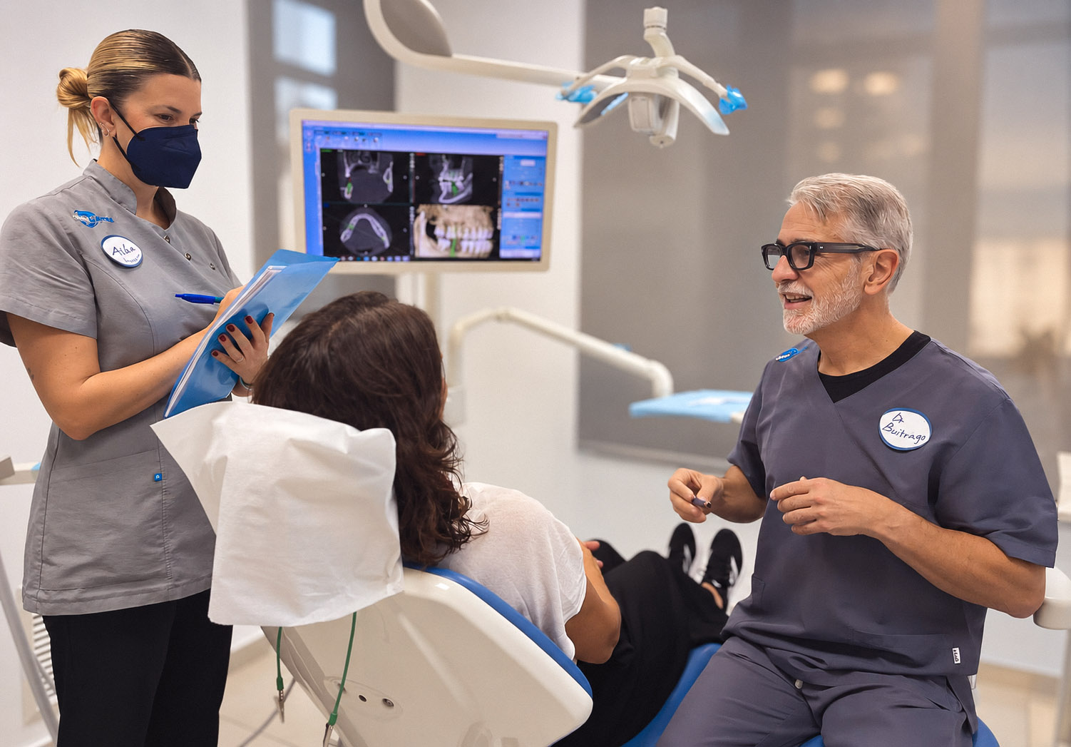 El Prof. Dr. Pedro Buitrago y la higienista Alba Escudero atienden a una paciente mientras revisan sus pruebas radiológicas durante una segunda opinión dental en Valencia